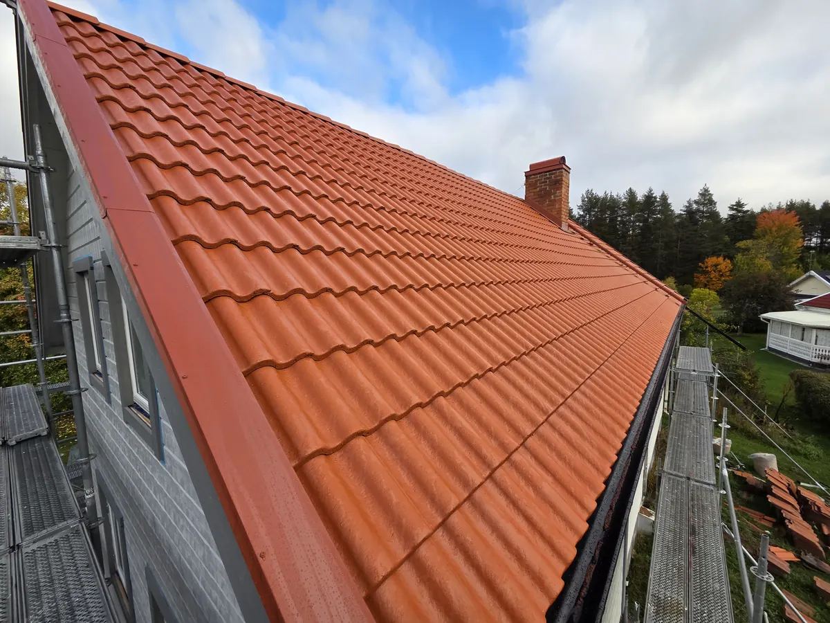 Nylagt tak med röda takpannor och ställning, med rivna pannor staplade på marken